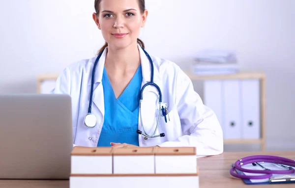 Schöne junge lächelnde Ärztin sitzt am Schreibtisch und schreibt — Stockfoto