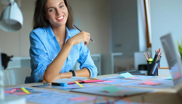 Jeune femme assise au bureau avec instruments, plan et ordinateur portable — Photo