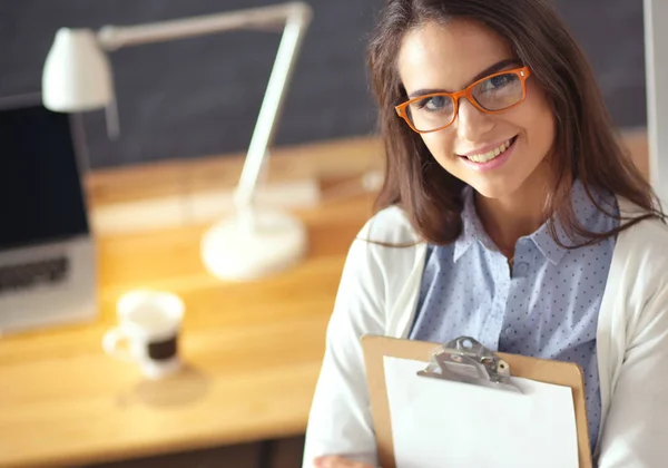 Mujer joven de pie cerca del escritorio con la carpeta de espera portátil —  Fotos de Stock