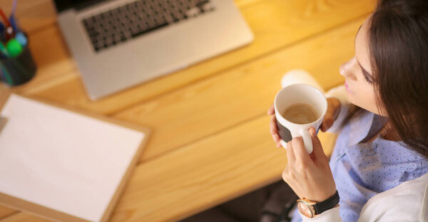 Портрет расслабленной молодой женщины, сидящей за столом с чашкой кофе