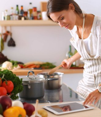 Mutfakta yemek yapmak için tablet bilgisayar kullanan genç bir kadın. .