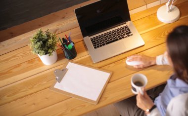 Portre rahat genç bir kadın masasında oturmuş elinde bir fincan kahve tutuyor.