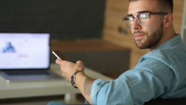 Genç adam kullanarak telefon ve dizüstü bilgisayarda çalışır.