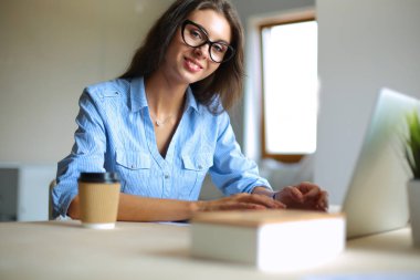 Ofis masasında dizüstü bilgisayarıyla oturan genç bir kadın.