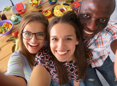 Öğle yemeği sırasında selfie çeken bir grup insan.