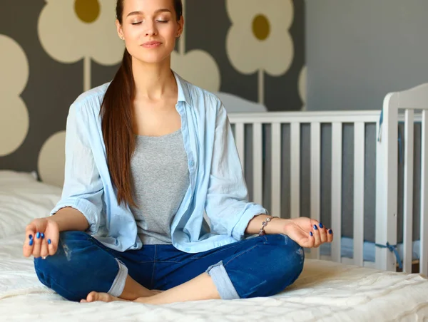 Young woman sitting on the bed near childrens cot. — Stock Photo, Image