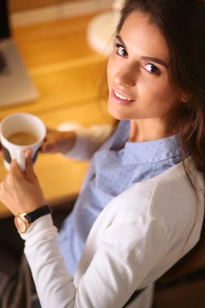 Porträtt avslappnad ung kvinna sitter vid sitt skrivbord håller kopp kaffe — Stockfoto