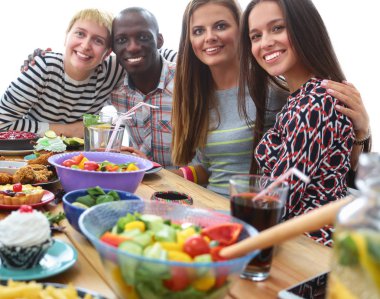 Bir grup insan ahşap masada otururken birlikte yemek yiyorlar.