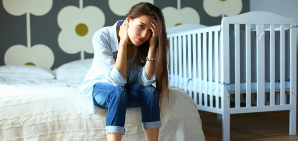 Junge müde Frau sitzt auf dem Bett neben Kinderbett — Stockfoto