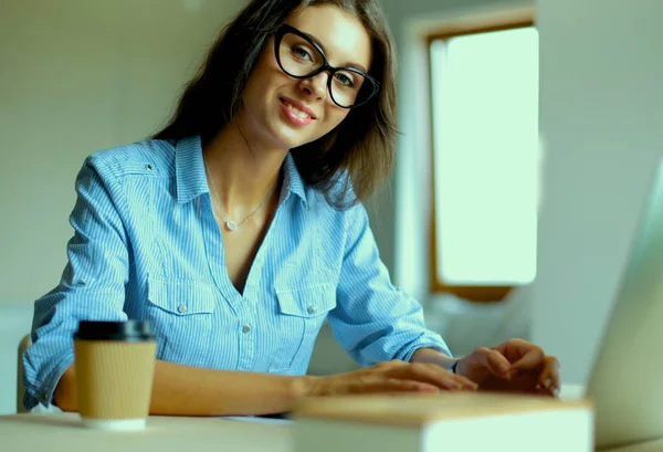 Ofis masasında dizüstü bilgisayarıyla oturan genç bir kadın. — Stok fotoğraf