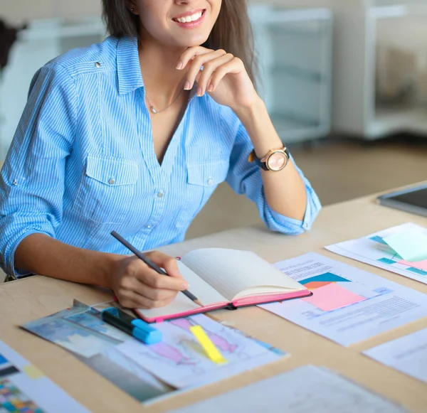 Jeune femme assise au bureau avec instruments, plan et ordinateur portable — Photo