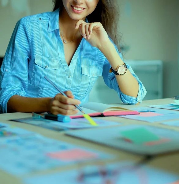 Masasında enstrümanlar, planlar ve dizüstü bilgisayarlarla oturan genç bir kadın.