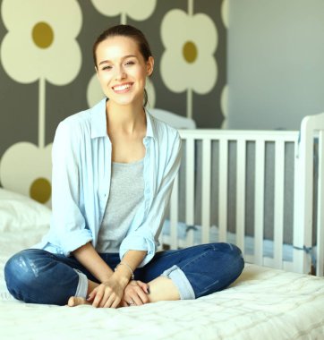 Yatakta çocuk karyolası yakın oturan genç kadın