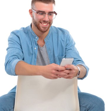 Sandalyede oturan ve cep telefonuyla genç adam