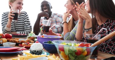 Bir grup insan ahşap masada otururken birlikte yemek yiyorlar.
