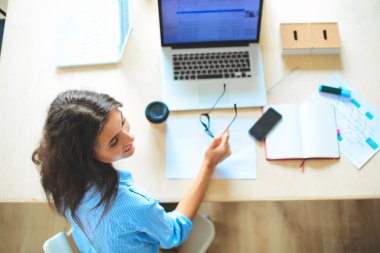 Dizüstü bilgisayar ekranına bakarak office tablosunda oturan genç kadın