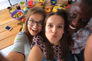 Öğle yemeği sırasında selfie çeken bir grup insan.