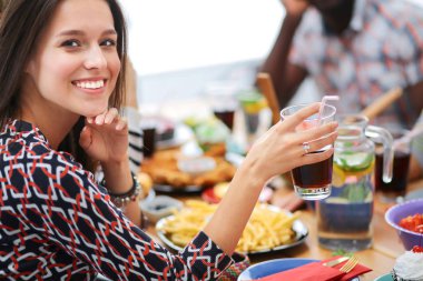 Bir grup insan ahşap masada otururken birlikte yemek yiyorlar.