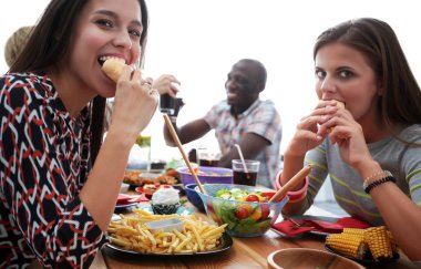 Bir grup insan ahşap masada otururken birlikte yemek yiyorlar.