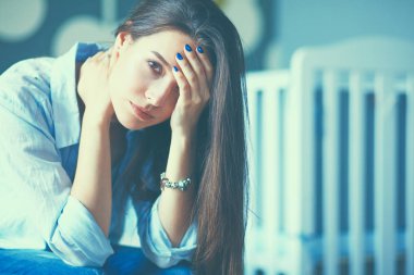 Yatakta çocuk karyolası yakın oturan genç yorgun kadın