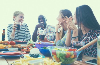 Bir grup insan ahşap masada otururken birlikte yemek yiyorlar.