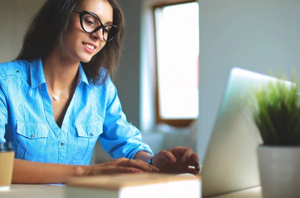 Jovem mulher sentada na mesa do escritório, olhando para a tela do computador portátil — Fotografia de Stock