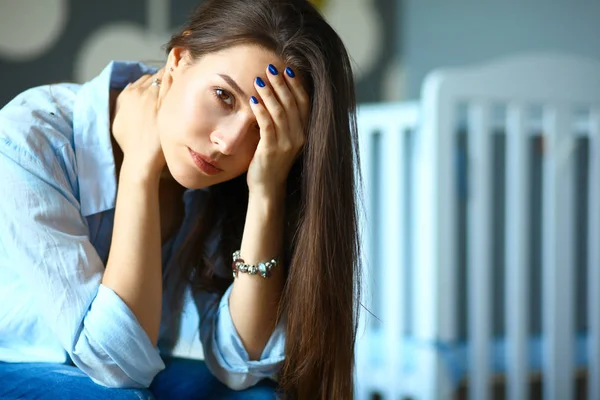 Mladá unavená žena sedící na posteli poblíž dětské postýlky — Stock fotografie