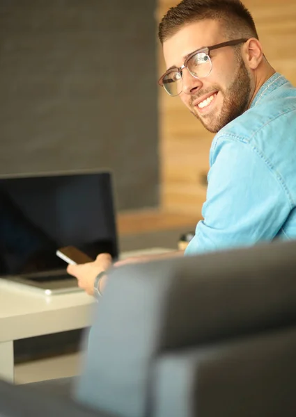 Młody człowiek przy użyciu telefonu i działa na laptopie — Zdjęcie stockowe
