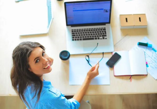Dizüstü bilgisayar ekranına bakarak office tablosunda oturan genç kadın — Stok fotoğraf