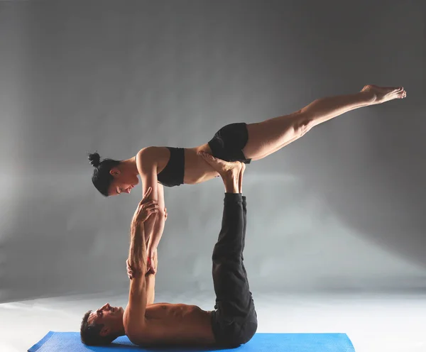 Casal jovem praticando acro ioga no tapete em estúdio juntos — Fotografia de Stock