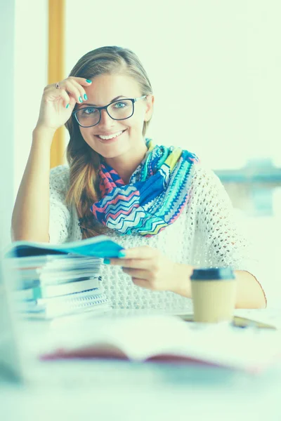 Jonge vrouw zit aan een bureau tussen de boeken — Stockfoto