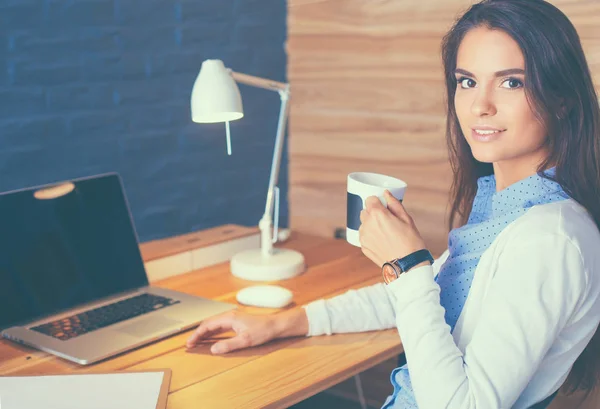 Porträt einer entspannten jungen Frau, die mit einer Tasse Kaffee an ihrem Schreibtisch sitzt — Stockfoto