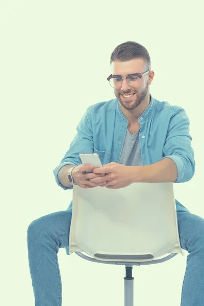 Ung man sitter på stol och med mobiltelefon — Stockfoto