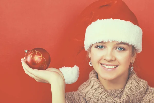 Mujer morena bonita en camisa y sombrero de santas sosteniendo bola roja de Navidad —  Fotos de Stock