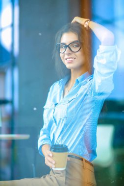 Ofis masasında dizüstü bilgisayarlı genç bir kadın oturuyor, pencereden bakıyor.