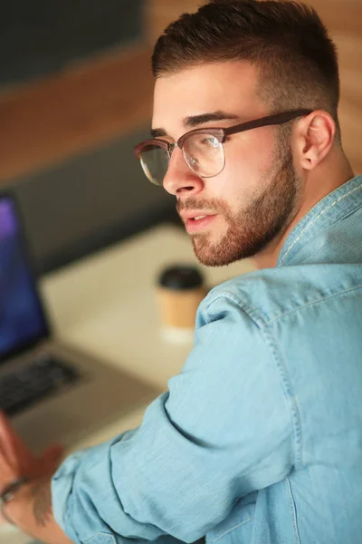 Ung man använder telefonen och fungerar på den bärbara datorn — Stockfoto