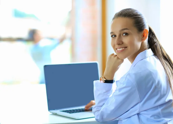 Bonito jovem sorridente médico feminino sentado na mesa — Fotografia de Stock