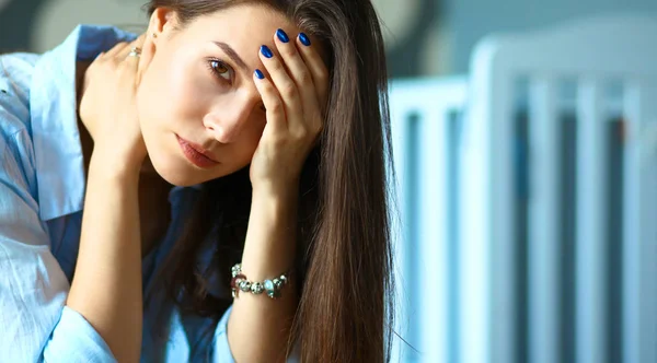 Young tired woman sitting on the bed near childrens cot — Stock Photo, Image