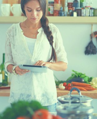 Mutfakta yemek yapmak için tablet bilgisayar kullanan genç bir kadın.