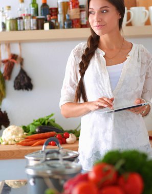 Mutfakta yemek yapmak için tablet bilgisayar kullanan genç bir kadın.
