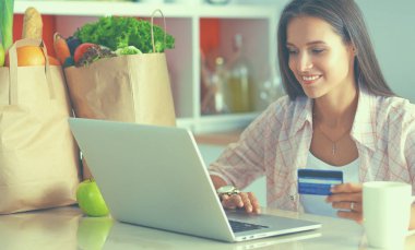 Gülümseyen kadın mutfakta tablet ve kredi kartı kullanarak alışveriş online