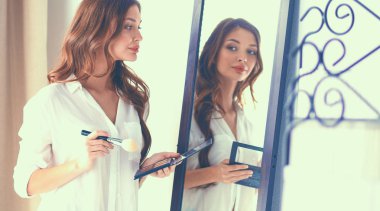 Genç ve güzel bir kadın aynanın yanında makyaj yapıyor.