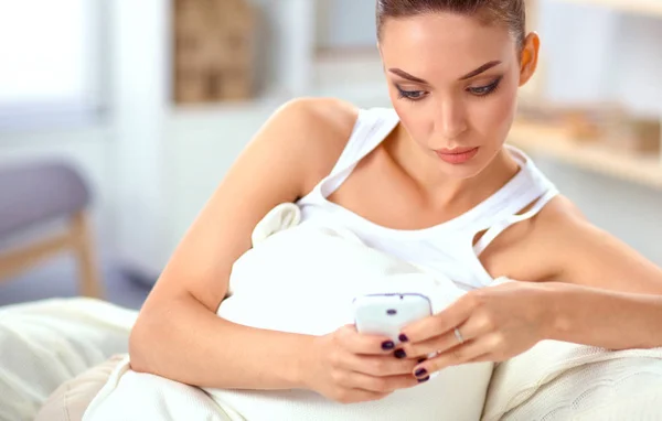 Молода красива жінка сидить на дивані у своїй кімнаті за допомогою телефону — стокове фото