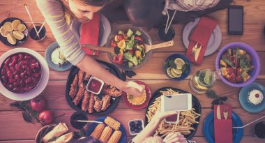 Bir grup insan ahşap masada otururken birlikte yemek yiyorlar.