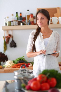 Mutfakta yemek yapmak için tablet bilgisayar kullanan genç bir kadın.