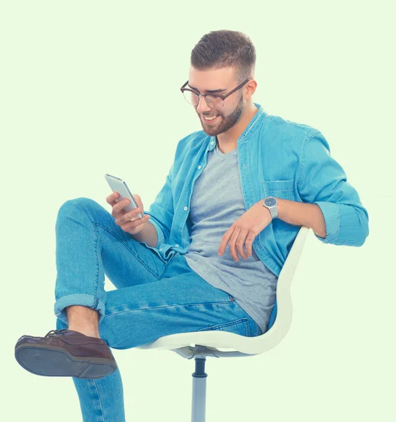 Ung man sitter på stol och med mobiltelefon — Stockfoto