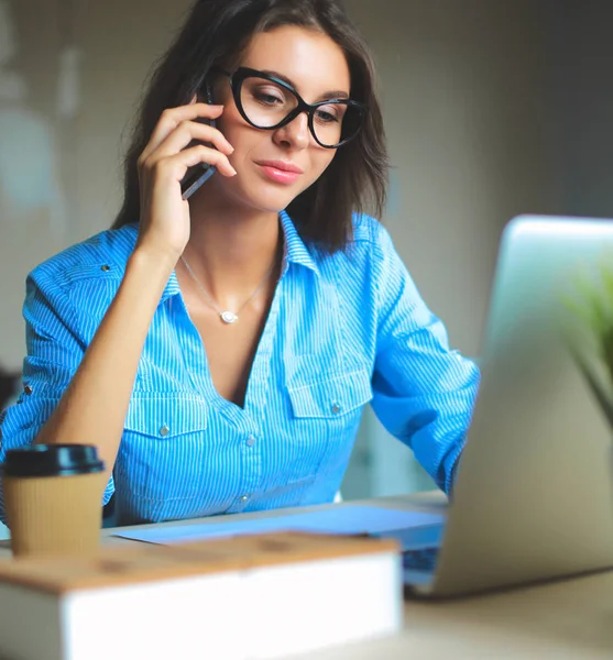 Vacker ung affärskvinna sitter vid skrivbordet och pratar på mobiltelefon — Stockfoto
