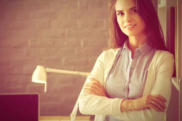 Jonge vrouw staat in de buurt van bureau met laptop — Stockfoto