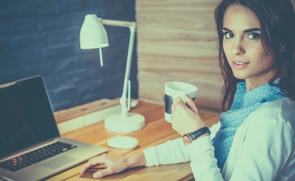 Porträt einer entspannten jungen Frau, die mit einer Tasse Kaffee an ihrem Schreibtisch sitzt — Stockfoto