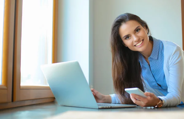 Jeune femme debout près du bureau avec ordinateur portable — Photo